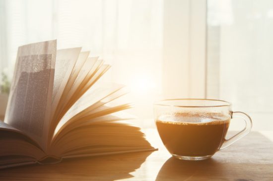 cup on morning coffee and open book on wooden table